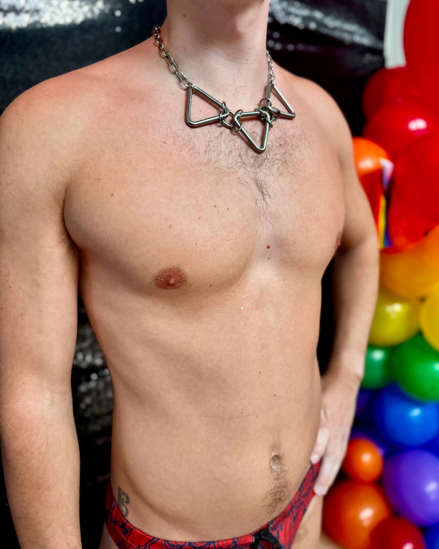 A person wearing a bold, geometric stainless steel necklace featuring three large, triangular links connected by chain rings. The necklace sits snugly on the person’s chest, showcasing the metallic design against bare skin.