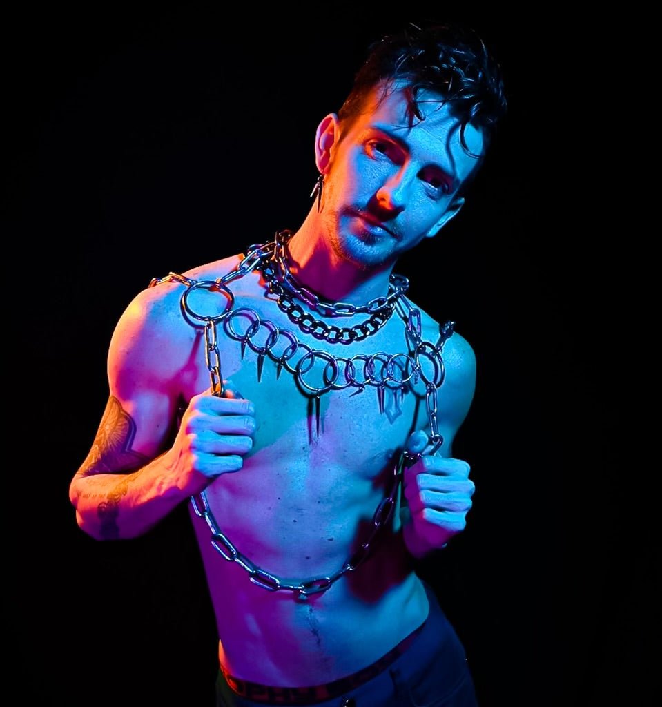 A person wearing a bold stainless steel body harness featuring an array of circular rings across the chest. The geometric design adds structure, while the layered chains create an industrial, artistic look. triangle necklace compliments this piece.