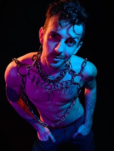 A person wearing a bold stainless steel body harness featuring an array of circular rings across the chest. The geometric design adds structure, while the layered chains create an industrial, artistic look. triangle necklace compliments this piece.