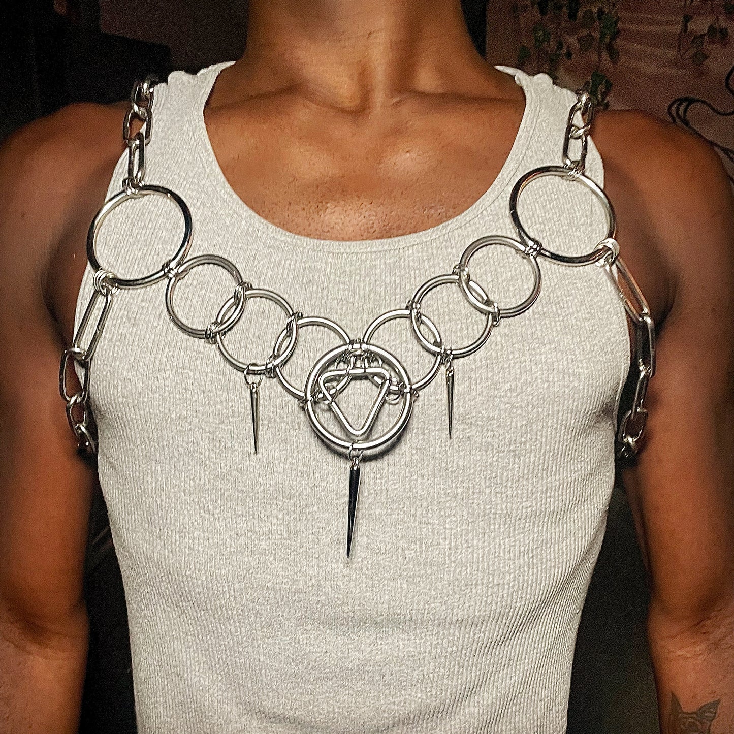 A person wearing a bold stainless steel body chain featuring an array of circular rings across the chest. A triangle sits in the middle and draws the eye. The geometric design adds structure, while the layered chains create an industrial, artistic look.