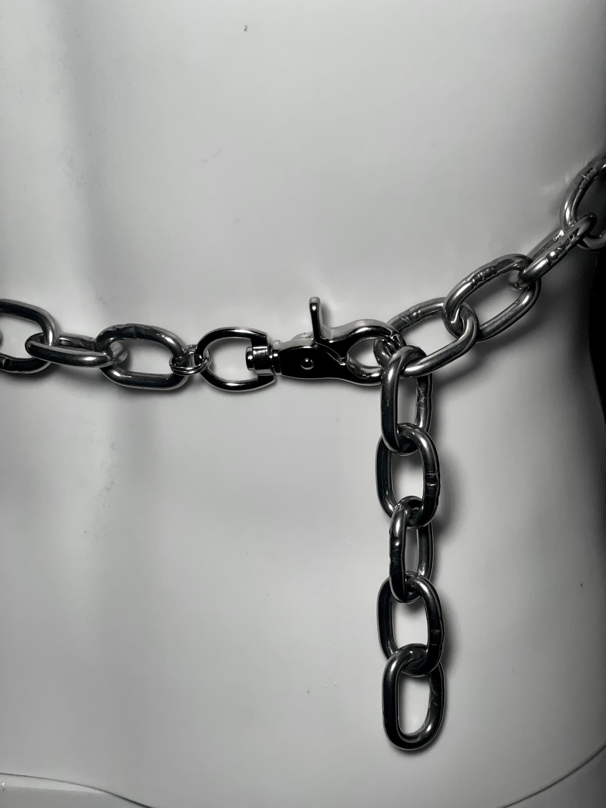 Close-up image of the back of a bold, handmade stainless steel chain harness featuring interlocking circular rings and thick metal links. This is finished off with a lobster claw.