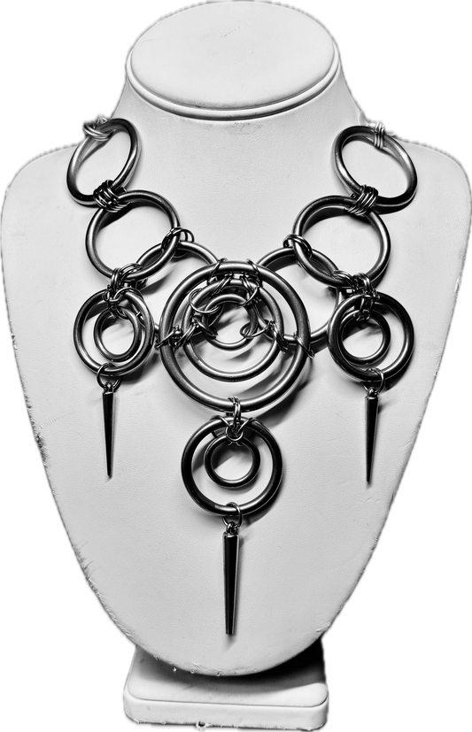 A stainless steel statement necklace featuring bold interlocking rings and three sharp, elongated spike pendants. The necklace has an industrial, edgy design, displayed on a white mannequin bust.