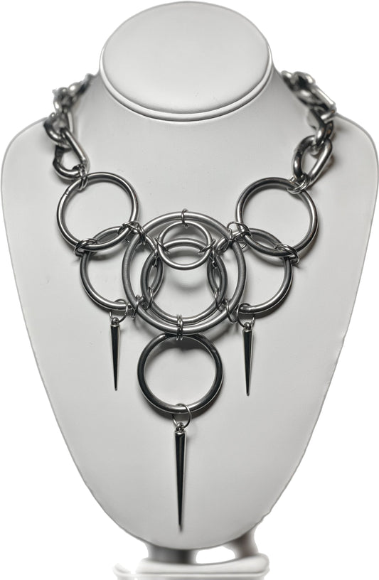 A bold stainless steel necklace made from interlocking cock rings and silver dagger accents, finished with a twisted link chain.