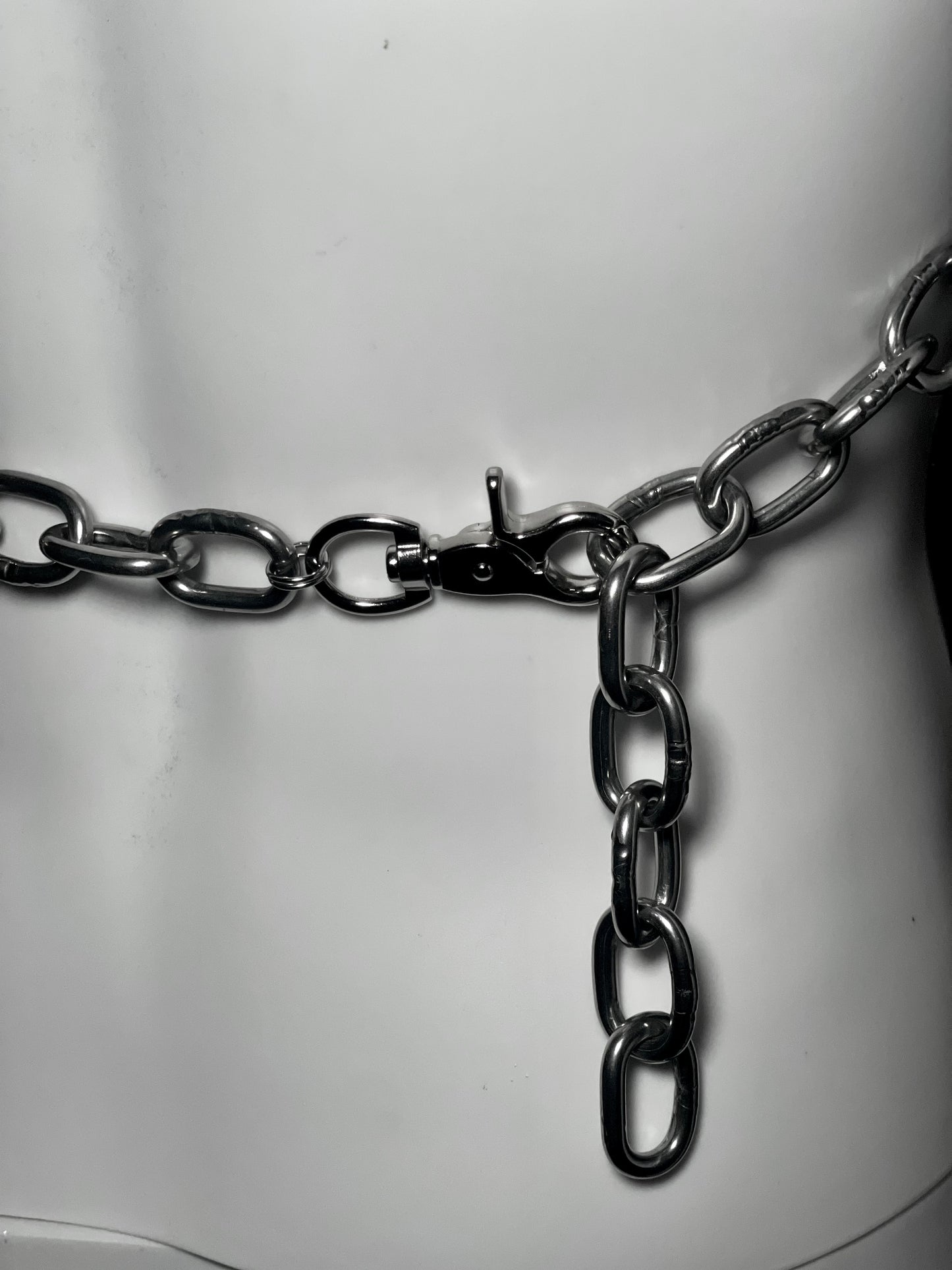 Close-up image of the back of a bold, handmade stainless steel chain harness featuring interlocking circular rings and thick metal links. This is finished off with a lobster claw. 